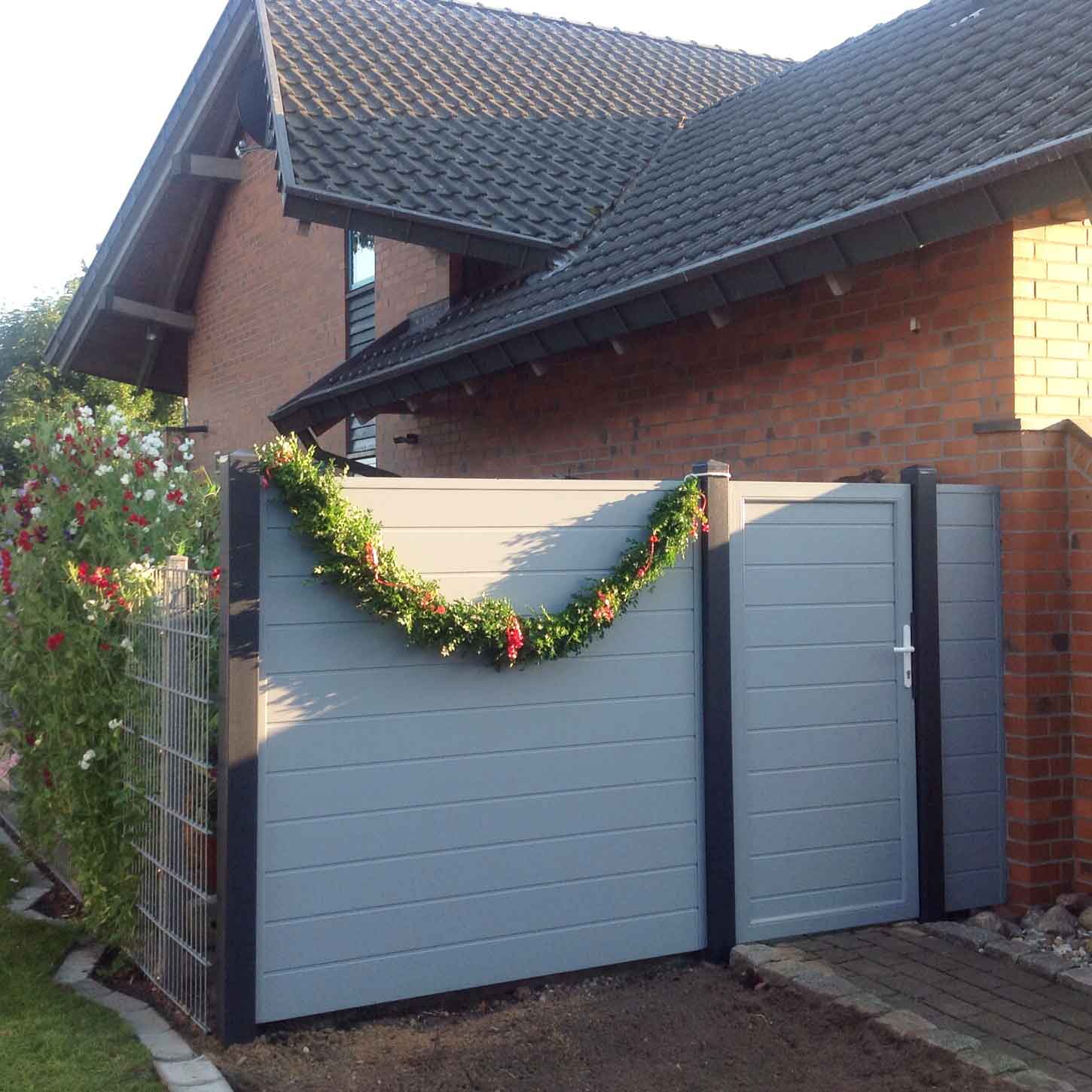 Sichtschutzwand mit integrierter Sichtschutztür aus Kunststoff in Grau auf einem Hof