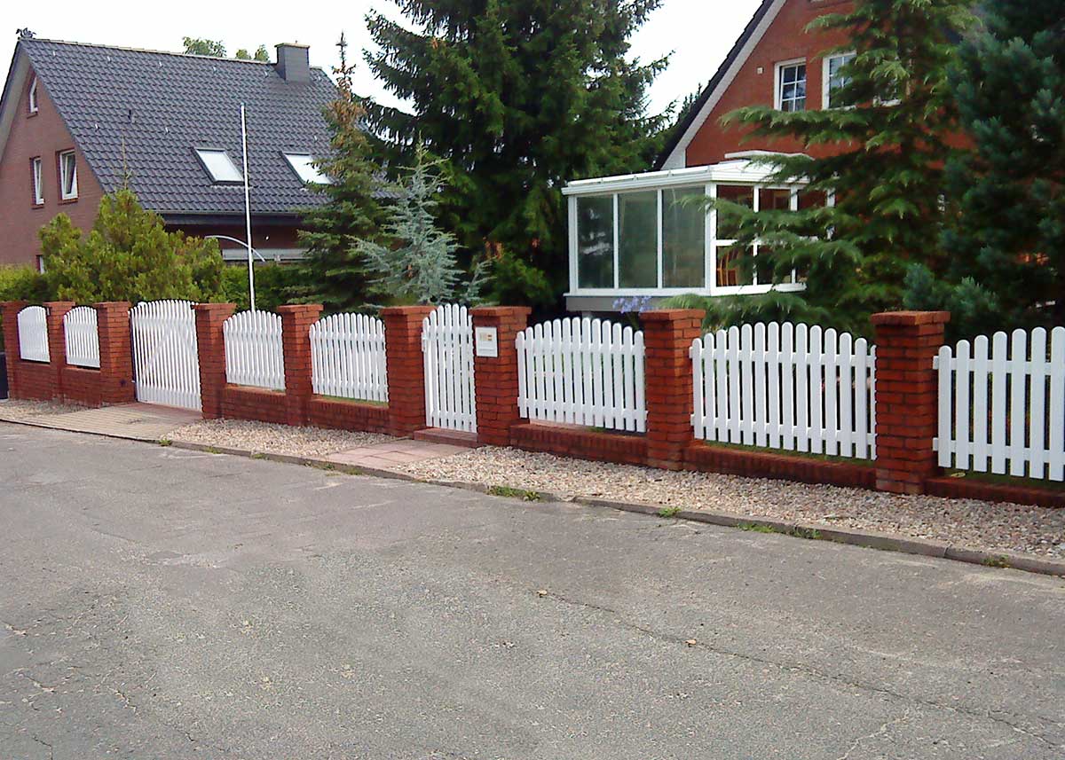 Lattenzaun Friesenzaun in Weiß aus hochwertigen Kunststoff mit Oberbogen, zwischen Ziegelmauer