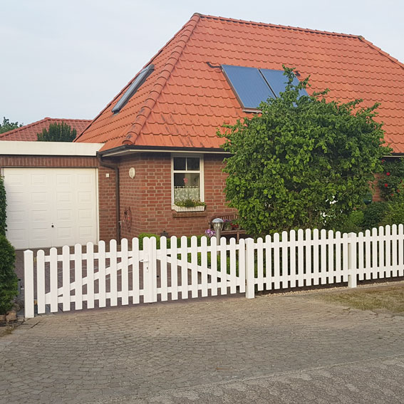 Lattenzaun mit Hoftor in weiß vor kleinem Einfamilienhaus